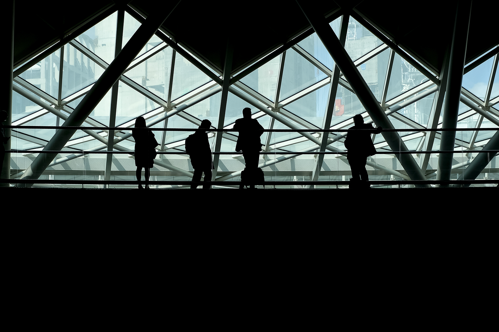 Silhouettes of people in modern architectural space with geometric glass ceiling representing collaboration and professional development